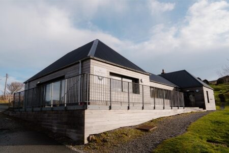 Timber-clad building with black roof and metal railings along a gravel path