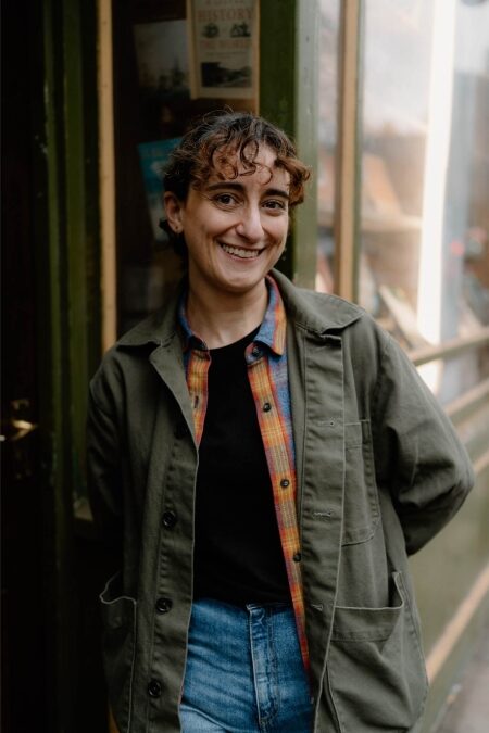 Woman in green jacket smiles beside a shop doorway with "History" poster