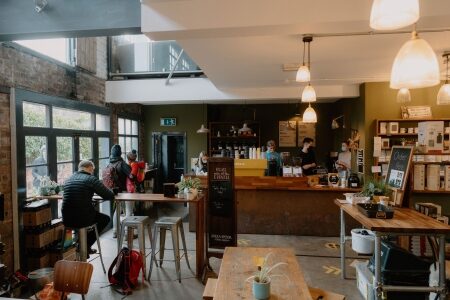 Customers queue at the counter inside a plant-filled café with exposed brick walls