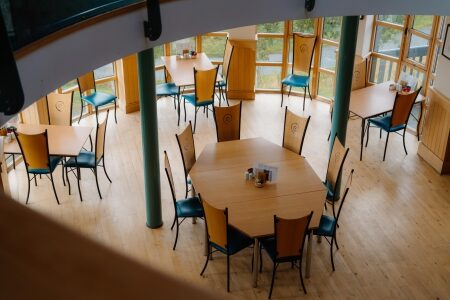 Wooden tables and blue-cushioned chairs seen from a curved upper balcony
