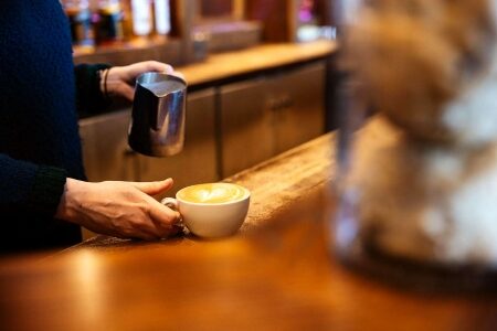 Barista pours milk into a latte at a wooden counter
