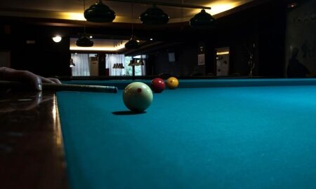 A pool table under low lamps in the Gabbro Bar, a ball about to be struck.