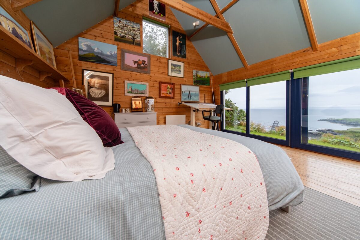 The studio at Half of One, Mark Gilbert's paintings covering the wooden wall above the bed, the sea through the glass doors.