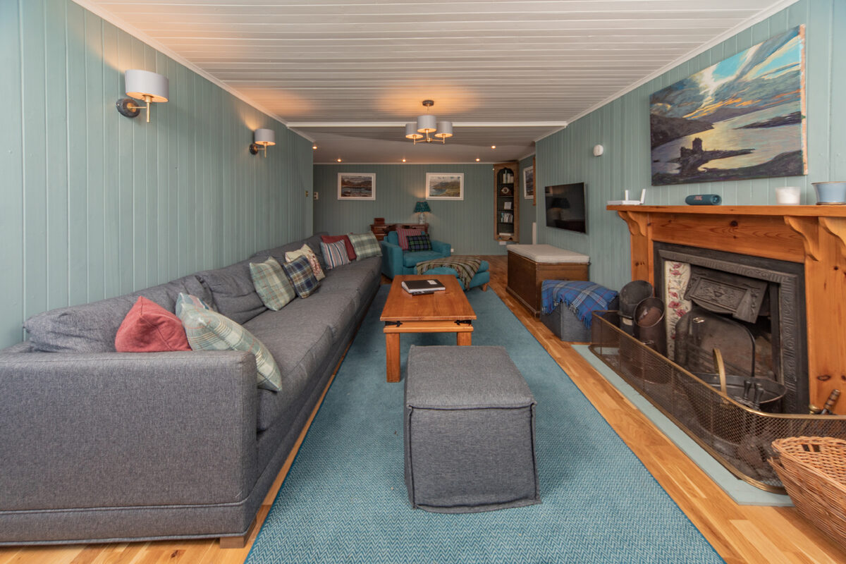 The long sitting room at Half of One, a grey sofa along one wall facing an open fireplace.