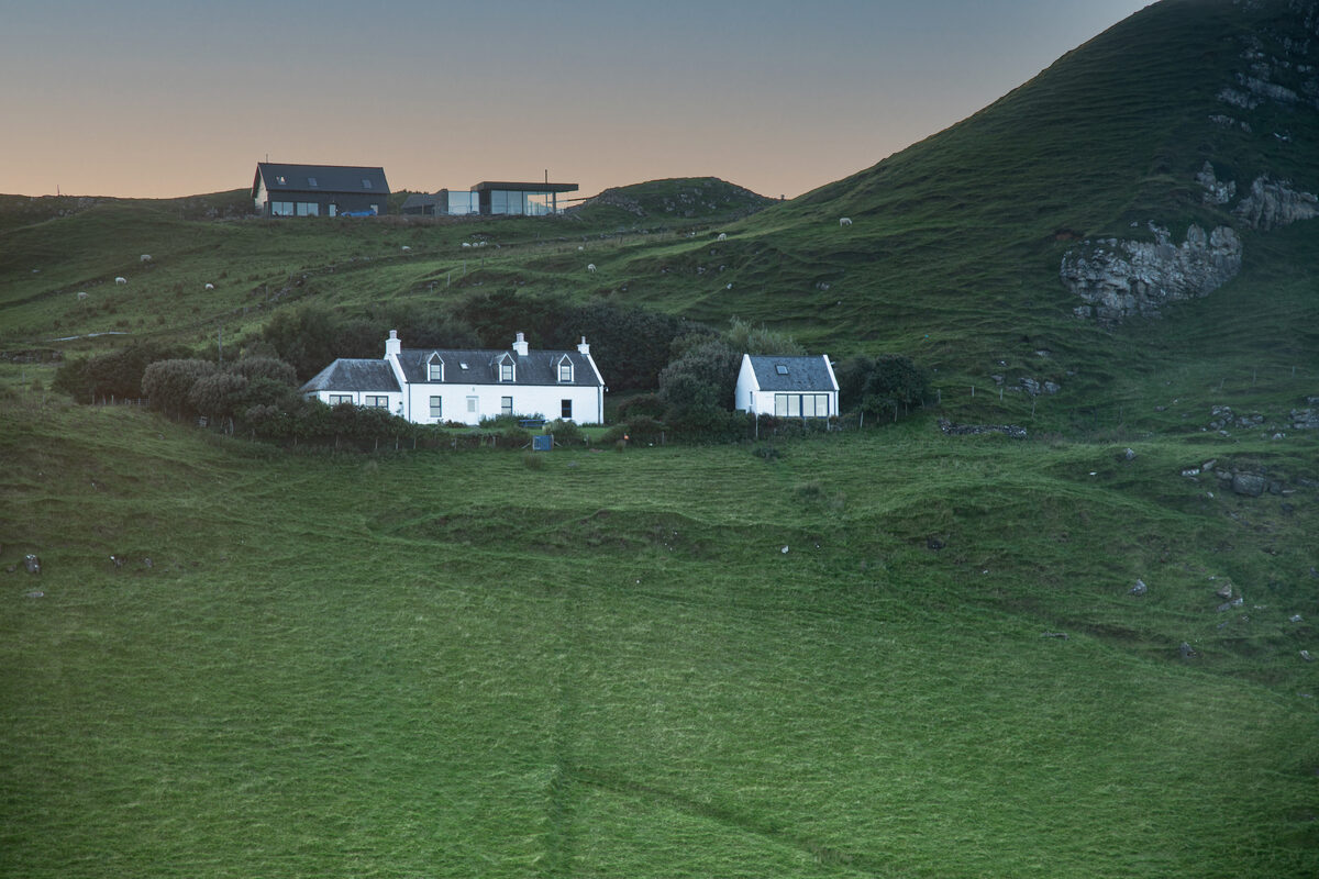 Half of One and its neighbour on the croft, two white cottages on a green hillside above the coast.