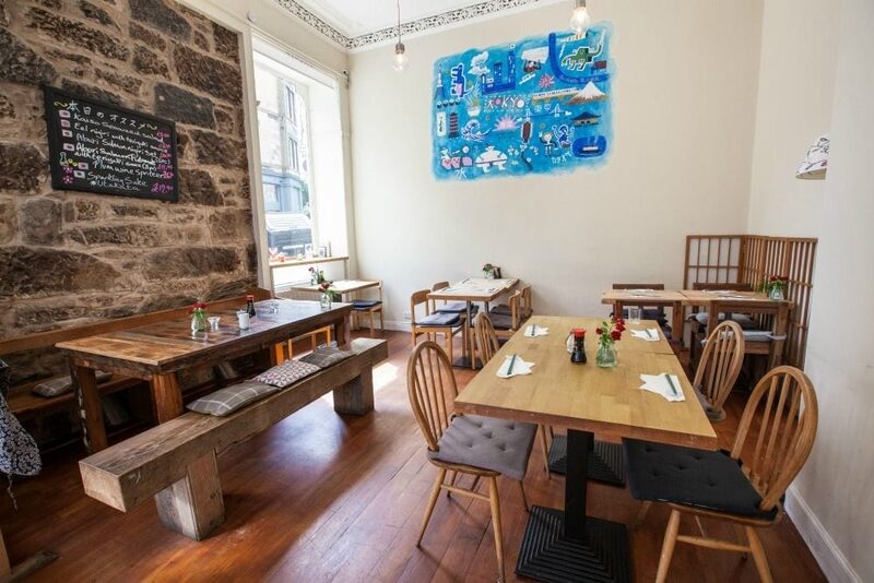 Wooden tables and benches beneath a blue artwork on a stone wall
