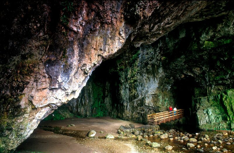 Wooden viewing platform inside a large cave with rocky floor and green-lit walls