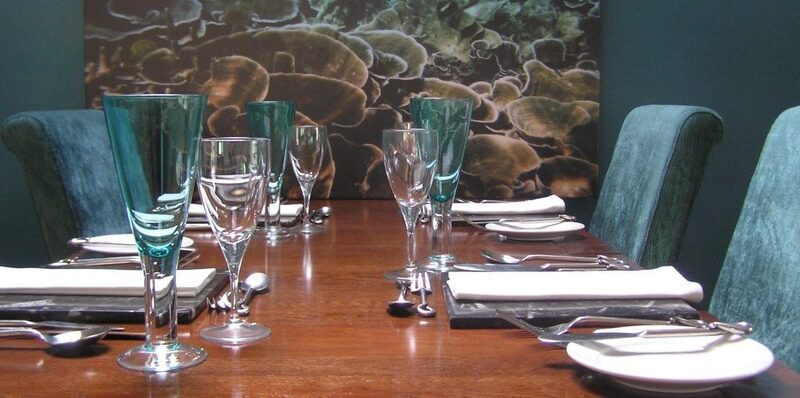 A table laid with glasses and white napkins at Ninth Wave, a painting of pebbles on the wall behind.