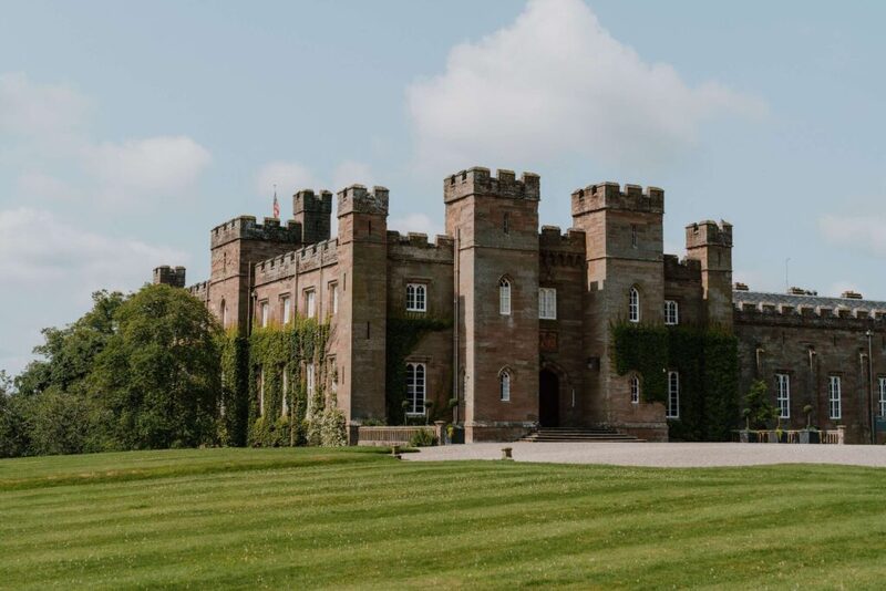 Turreted sandstone castle with crenellated towers overlooking a wide lawn