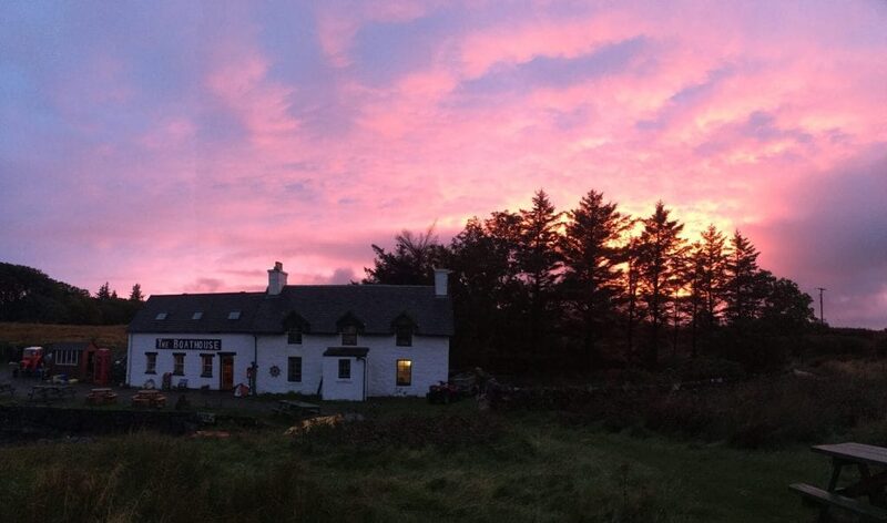 The white Boathouse on Ulva under a pink sunset sky, dark pines behind.
