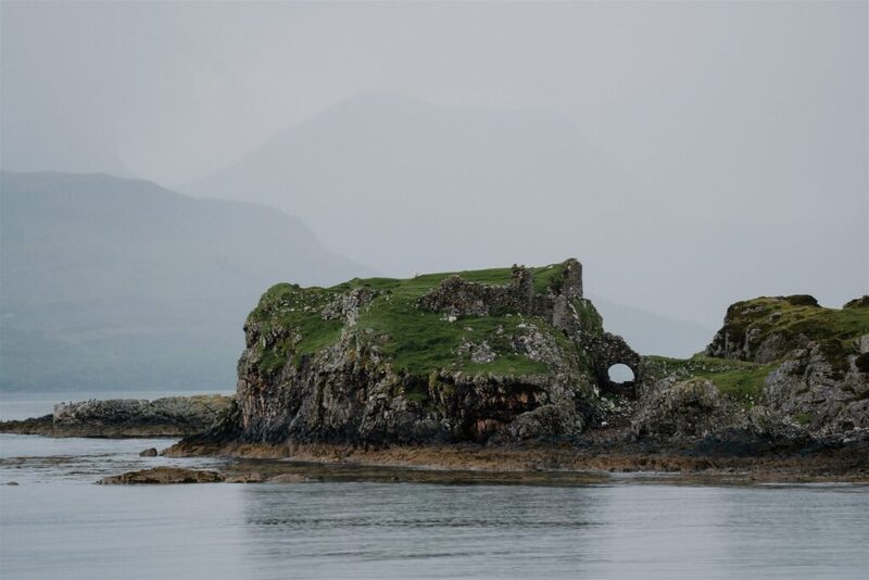 Grass-topped rocky islet with a natural arch, misty hills beyond