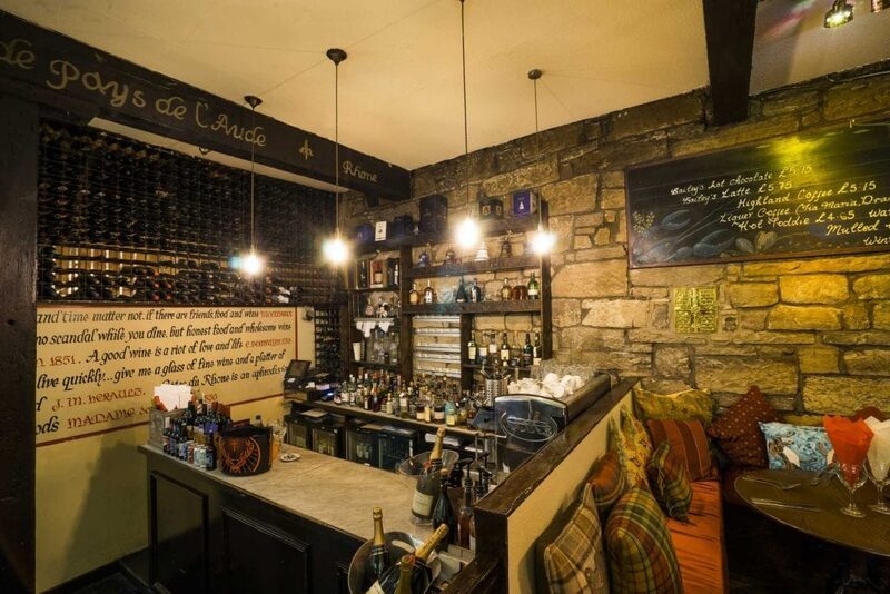 Stone-walled bar with wine racks, hanging lights and tartan cushioned seating