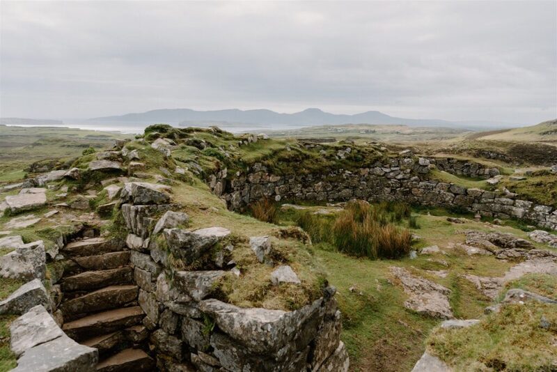 Stone stairway and ruined walls overlooking a coastline with distant hills