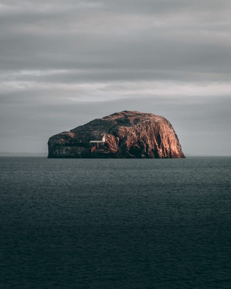Bass Rock rises from grey sea, its white lighthouse visible on the slope