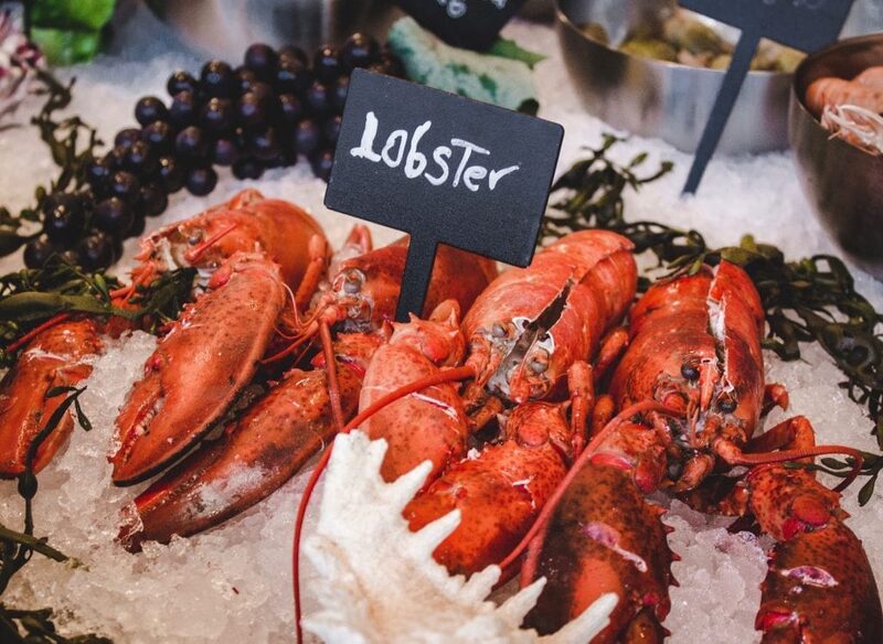 Whole lobsters on ice beside a chalkboard sign reading "lobster