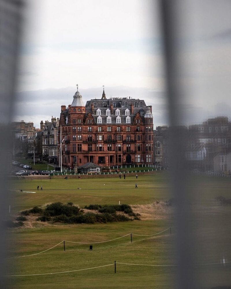 Red sandstone hotel overlooking St Andrews golf links, seen through railings