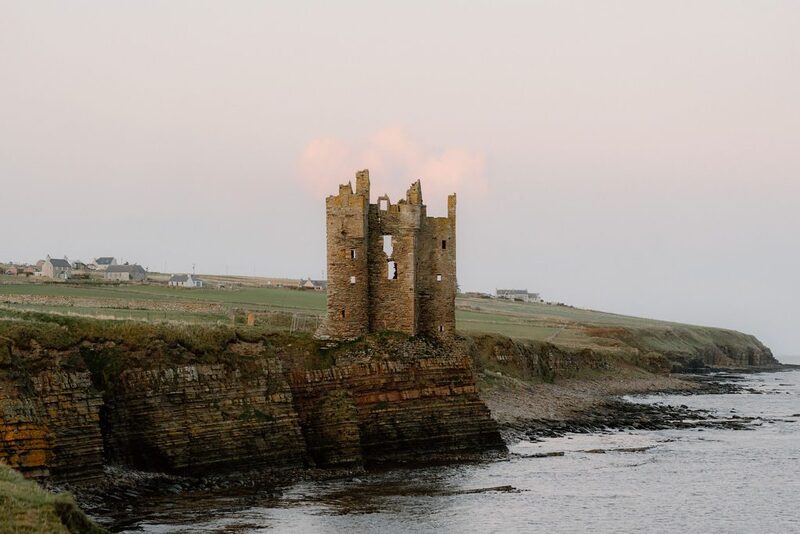 Ruined castle towers atop layered rock cliffs above the sea
