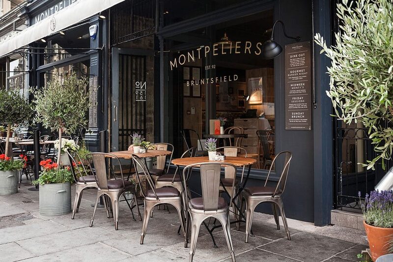 Metal tables and chairs outside Montpeliers Bruntsfield, with potted olive trees