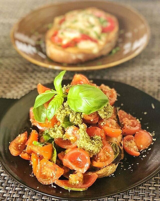 Bruschetta topped with cherry tomatoes, pesto and basil on black plates