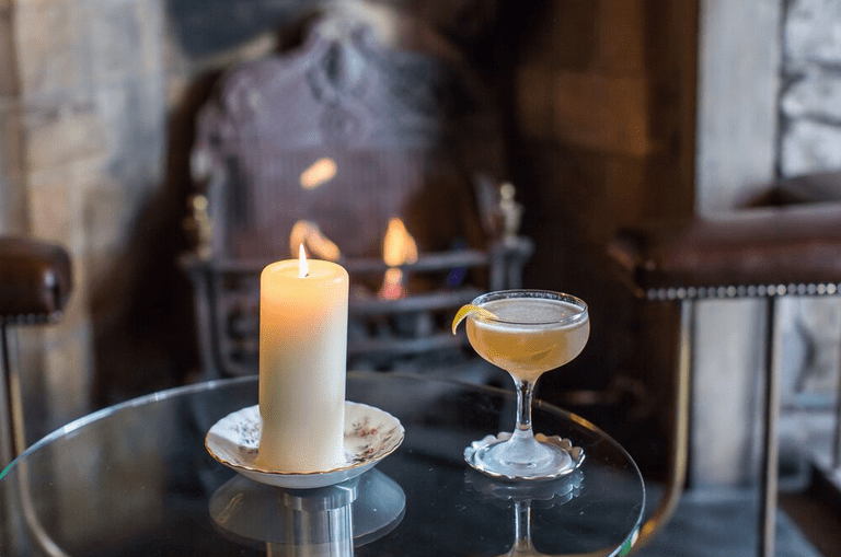 Candle and cocktail on a glass table beside an open fireplace