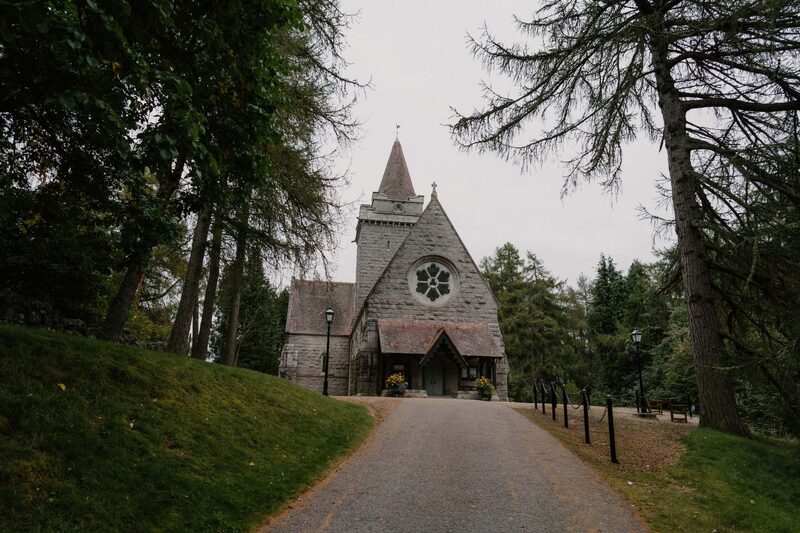 Stone church with spire and rose window at end of tree-lined drive