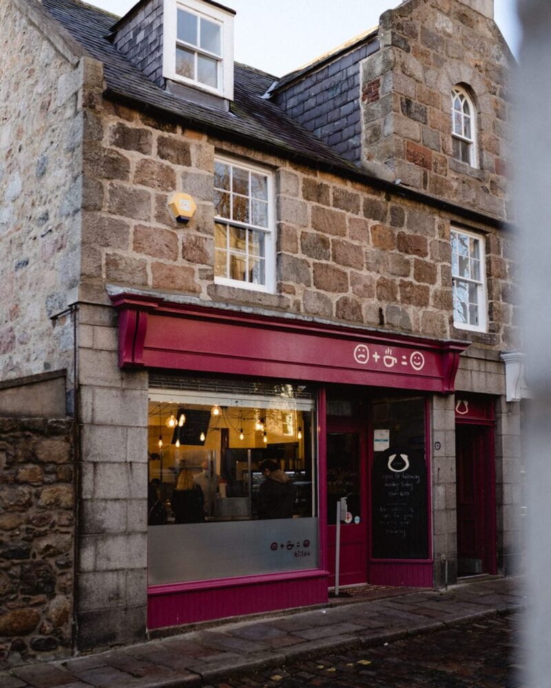 Granite building with a maroon-fronted café on a cobbled corner street