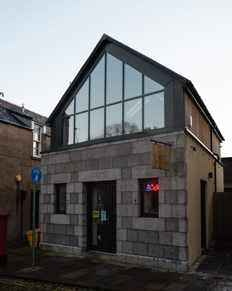 Granite building with glass gable extension and neon "Café" sign