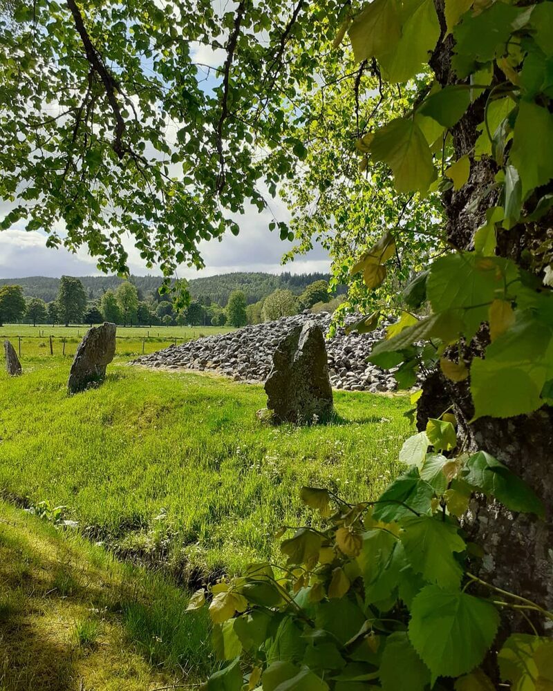 Standing stones and cairn at Balnuaran of Clava, framed by tree leaves