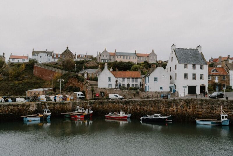 Fishing boats moored in Crail harbour beneath rows of white and orange-roofed cottages