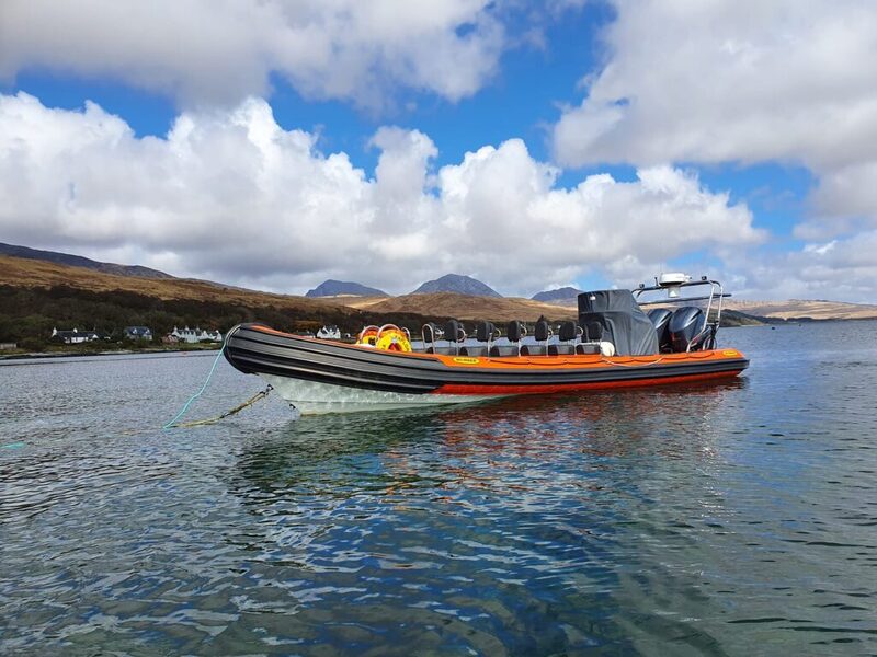 Orange and black rigid inflatable boat crossing calm water below distant hills