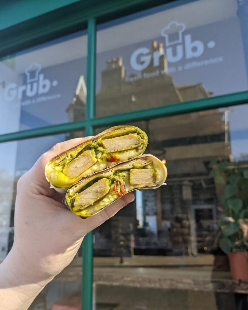 A hand holds a halved wrap outside Grub, "real food with a difference
