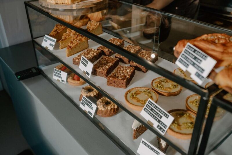 Glass bakery display with tarts, brownies and pastries on labelled shelves