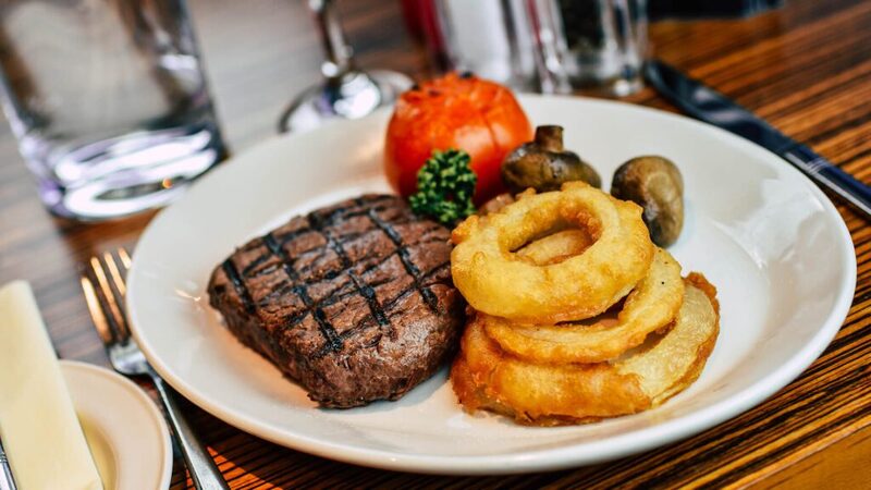 Grilled steak with onion rings, grilled tomato and mushrooms on a white plate