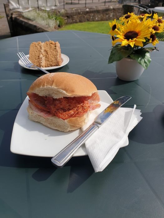 Bacon roll and cake on an outdoor table with sunflowers