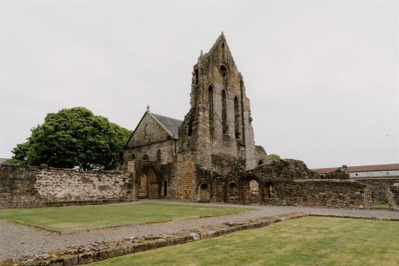 Ruined stone abbey tower and arched cloisters beside a mown lawn
