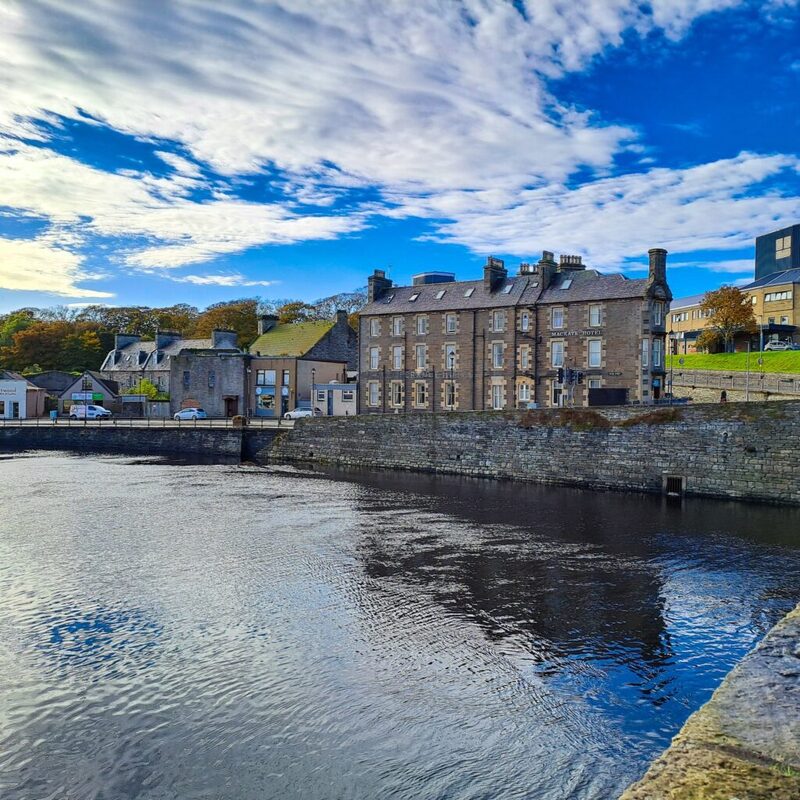 Sandstone buildings line the harbour wall beside calm water under a wide sky