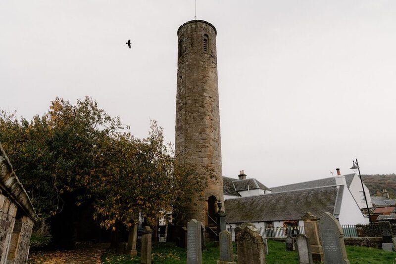 Round stone tower rising above a graveyard with a bird flying overhead
