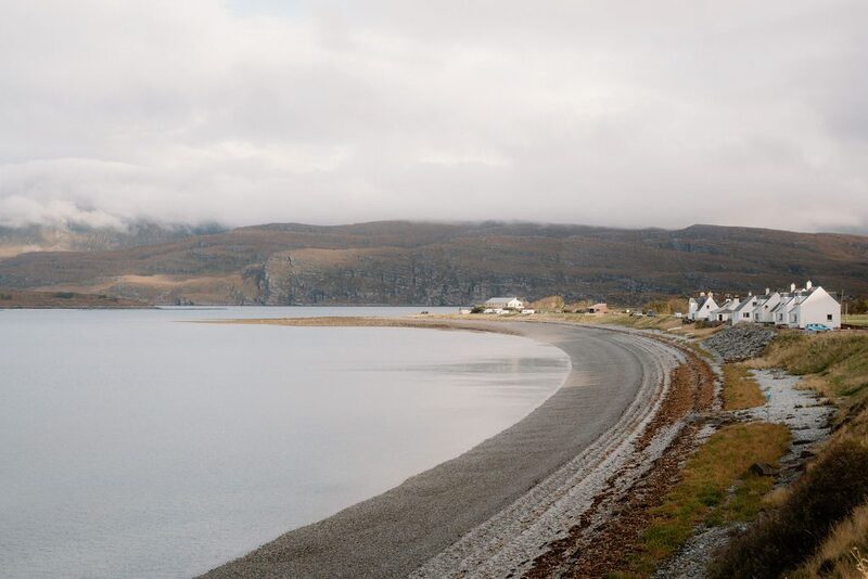Curved shingle beach beside white cottages, hills rising under cloudy skies