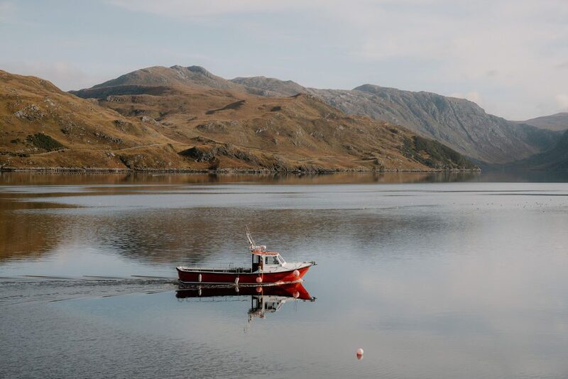 Red and white boat moored on a still loch beneath hills