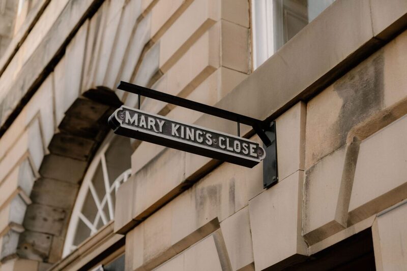 Black and white "Mary King's Close" sign mounted on sandstone building