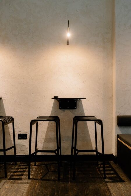 Black metal stools beneath a small wall lamp on textured plaster
