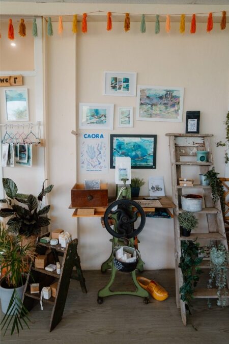 Framed seascapes, a "CAORA" print and vintage mangle fill this plant-lined shop corner
