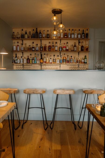 Wooden bar stools face shelves stacked with whisky bottles and hanging glass pendant lights