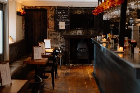 Wood burner between exposed stone walls in a pub with a bar and menus on tables