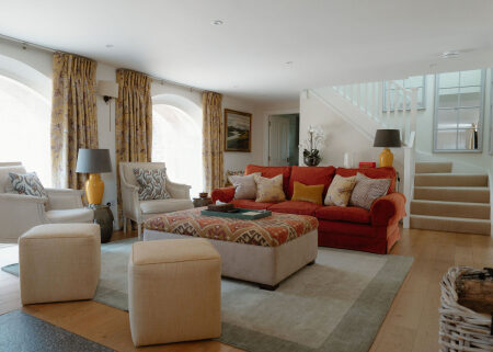 Living room with red sofa, patterned ottoman and staircase behind